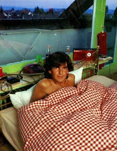 a man laying in bed under a red and white checkered blanket