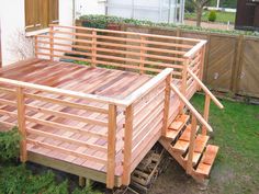 a wooden deck with steps leading up to the top and bottom part, in front of a house