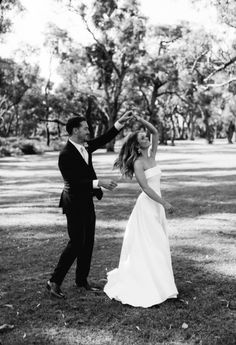 a bride and groom walking through the park together in black and white, holding hands with each other