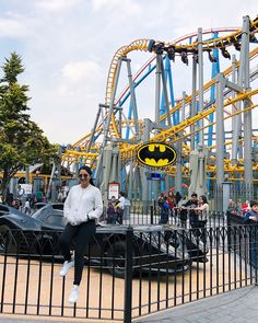 a woman sitting on top of a black car in front of a batman coaster at an amusement park