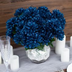 a vase filled with blue flowers sitting on top of a table next to white candles