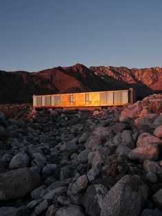 a house on top of rocks in the middle of a mountain range at dusk with mountains in the background