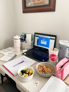 a laptop computer sitting on top of a white desk next to a bowl of fruit