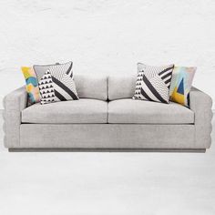 a gray couch with colorful pillows on it and a white wall in the back ground