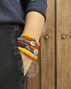 a person wearing colorful bracelets with an evil eye on their wrist and holding onto a wooden fence