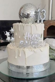 a white cake with silver decorations and a disco ball on top is sitting on a glass table