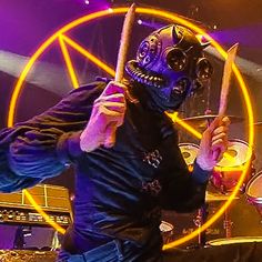 a man with a weird mask holding a drum stick