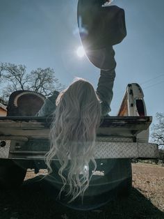 a woman with long hair sitting in the back of a pick up truck under a blue sky