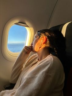 a woman is sitting in an airplane and looking out the window at the ocean below