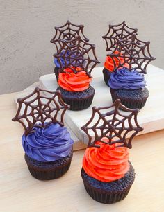 cupcakes decorated with chocolate icing and spooky spider web decorations on a cutting board