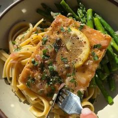 a person is holding a fork over a plate of pasta with asparagus and lemon