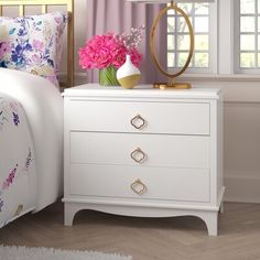 a white nightstand with pink flowers on it next to a bed and window sill