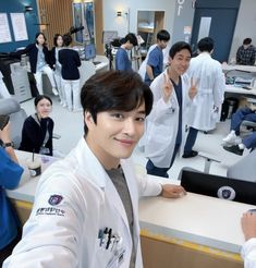 a man in white lab coat standing next to a counter with other people behind him