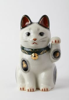 a white cat figurine with black and gold decorations on it's chest