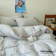 an unmade bed with white and blue checkered comforter, pillows and pictures on the wall