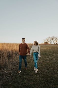 a man and woman holding hands walking through a field