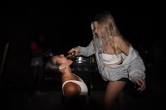 two women are cooking in the kitchen at night, one is bending over to eat