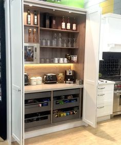 an open cabinet in the kitchen with wine bottles and other items on shelves next to it