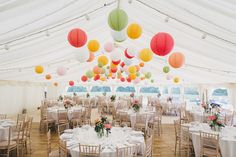 tables and chairs are set up in a tent with paper lanterns hanging from the ceiling