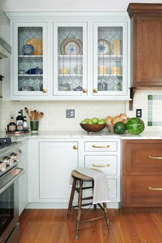 a kitchen with white cabinets and wood floors, including a wooden stool in front of the counter