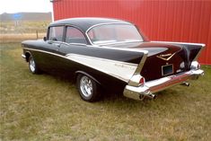 an old black and white car parked in front of a red building on the grass