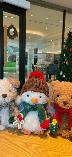 four teddy bears wearing hats and scarves are sitting on a table in front of a christmas tree