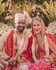 a man and woman sitting next to each other in front of some flowers on the ground