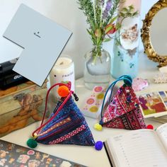 three small triangle shaped purses sitting on top of a table next to an open book