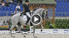 a woman riding on the back of a gray horse in an arena with people watching