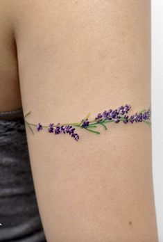 a woman's arm with purple flowers on it and green stems attached to the arm