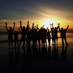 a group of people standing on top of a beach under a sun set with their arms in the air