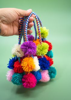 a hand holding a multicolored pom - pom bag on a green surface