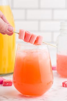 someone holding a toothpick over a drink in a glass with watermelon