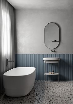 a white bath tub sitting next to a sink in a bathroom under a round mirror