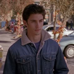 a young man in a denim jacket is standing on the street