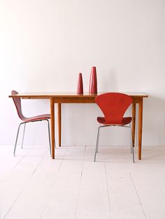 two red chairs sitting at a table with a vase on top of it and another chair next to the table