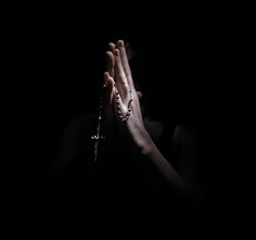 a woman is praying in the dark with her hands folded up and rosarys around her