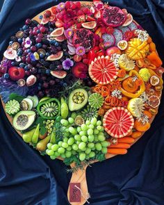 a large plate filled with lots of different types of fruits and vegetables on top of a blue cloth