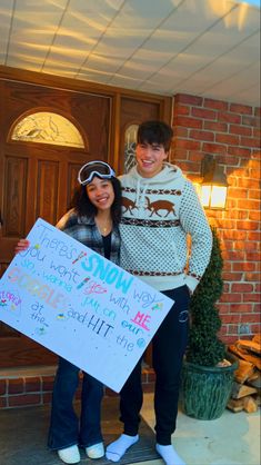 a man and woman standing in front of a door holding a sign that says snow