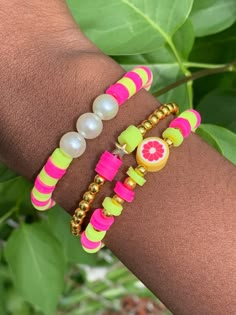 two bracelets with fruit charms and pearls on each one hand, sitting in front of green leaves