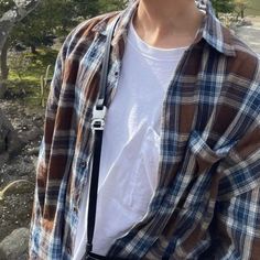 a young man wearing glasses and a plaid shirt is standing in front of some trees