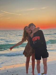 two people are hugging on the beach at sunset