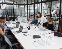 a group of people sitting around a table with laptops on it and papers in front of them