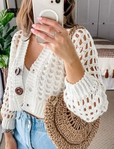 a woman taking a selfie with her cell phone while wearing a white sweater and jeans