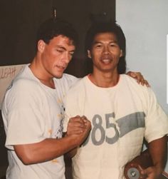 two men standing next to each other with their arms around one another and looking at the camera