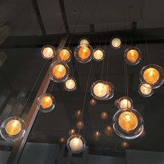 several lit candles are hanging from the ceiling in a circle with glass bowls on it