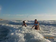 two women in bikinis wading out into the ocean