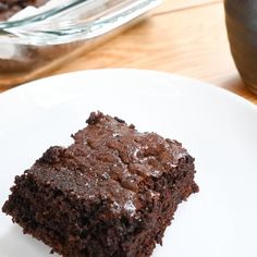 a piece of chocolate cake sitting on top of a white plate next to a glass container