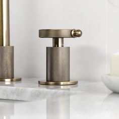 two bathroom faucets on a marble countertop next to a white candle holder