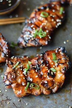 grilled chicken with sesame seeds and green onions on a sheet of tin foil next to chopsticks